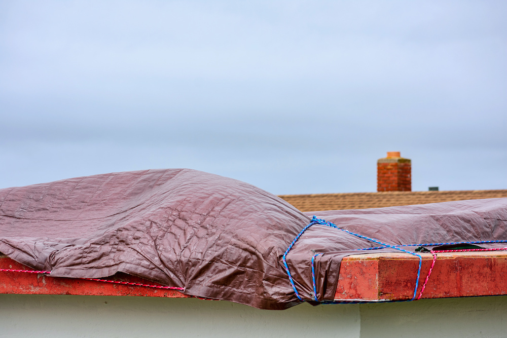 A house has a tarp over the roof so that an emergency roof repair may be done.